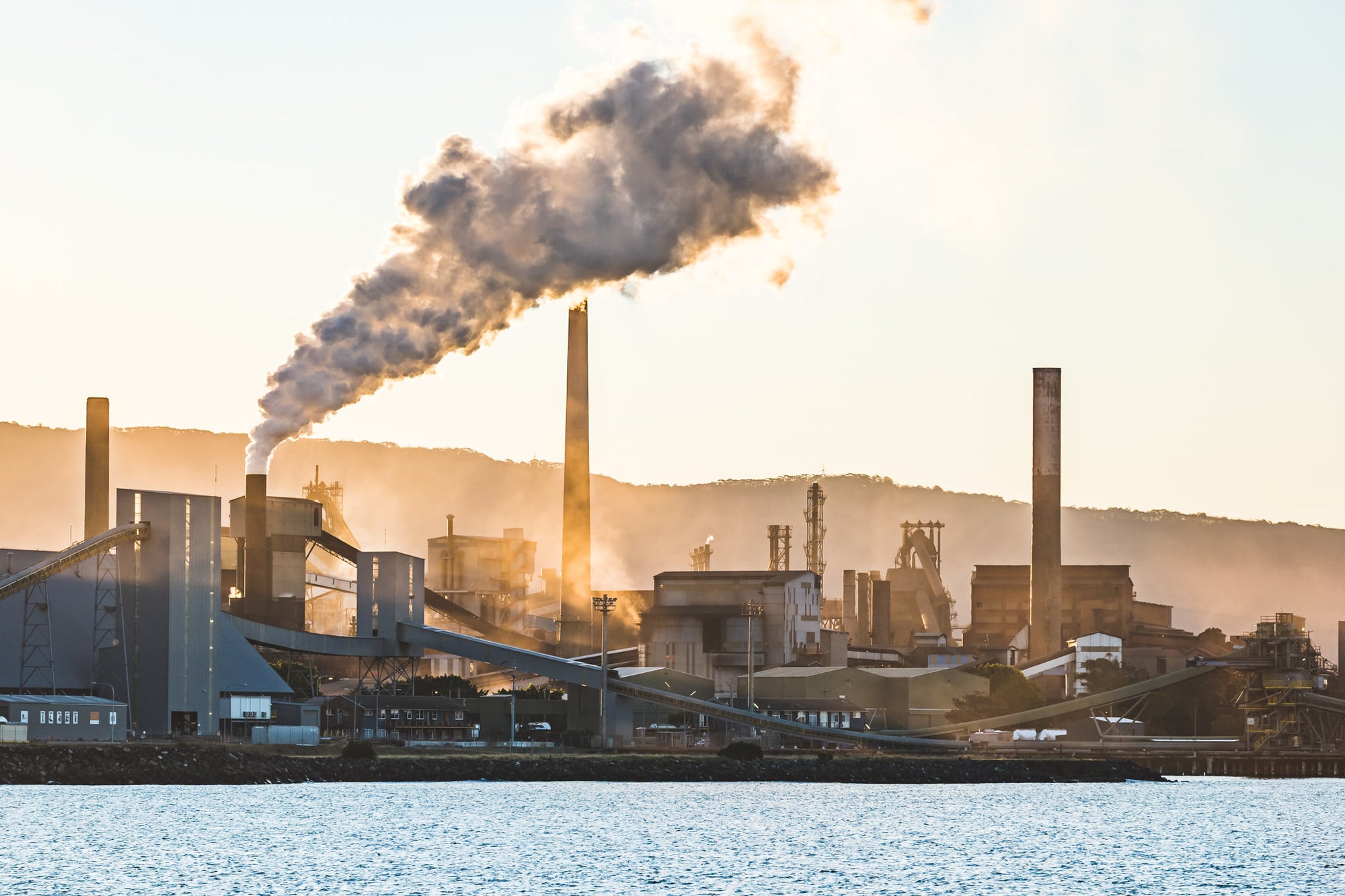 Port Kembla Sunset at BlueScope Port Kembla, smoke pours from a tall stack and drifts south across the steelworks skyline.