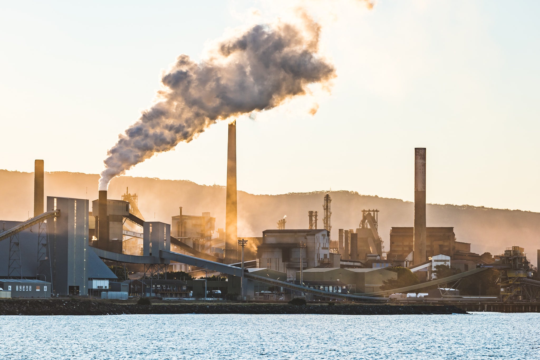 Port Kembla Sunset at BlueScope Port Kembla, smoke pours from a tall stack and drifts south across the steelworks skyline.