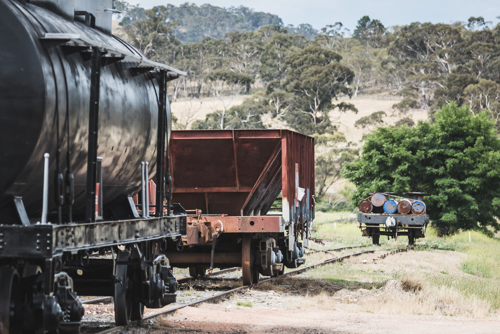 L Truck at Bombala Station, a black cylindrical tank wagon sits coupled to a rust-red hopper truck on a siding of worn rail.