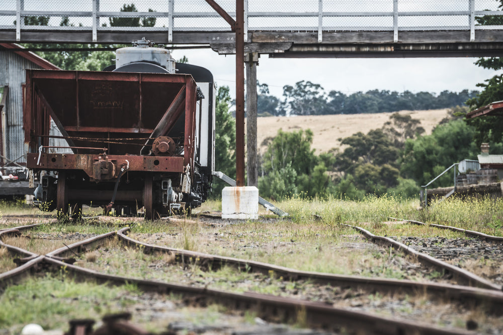 Upline at Bombala Station, a rusted hopper wagon sits low on the sidings beneath a steel and timber footbridge.