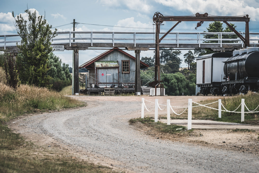 Yard at Bombala Station, a gravel road curves beneath a steel overhead crane and timber footbridge.