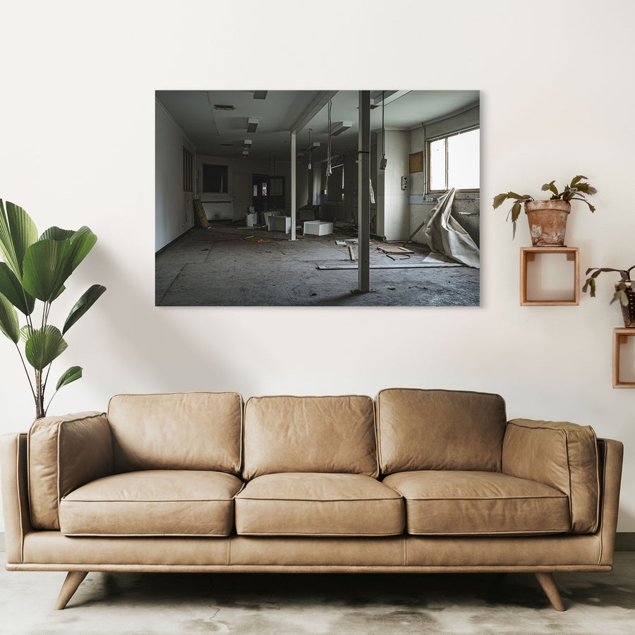 Stripped interior room at the former Bradmill factory in Yarraville, with a white support column, scattered cabinetry panels and cables on a bare concrete floor, and daylight entering from a window on the right.