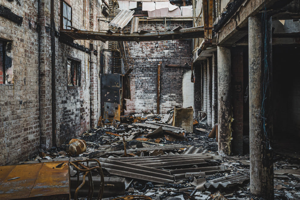 Gutted brick interior of a fire-damaged manufacturing building at the former Bradmill factory in Yarraville, with charred debris on the floor, soot-stained walls and exposed steel framing overhead.