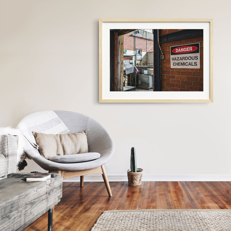 A weathered "Danger Hazardous Chemicals" sign on a brick wall beside an open timber doorway at the former Davies Coop / Bradmill factory in Yarraville, with metal cabinets, storage racks and an illuminated exit sign visible inside.