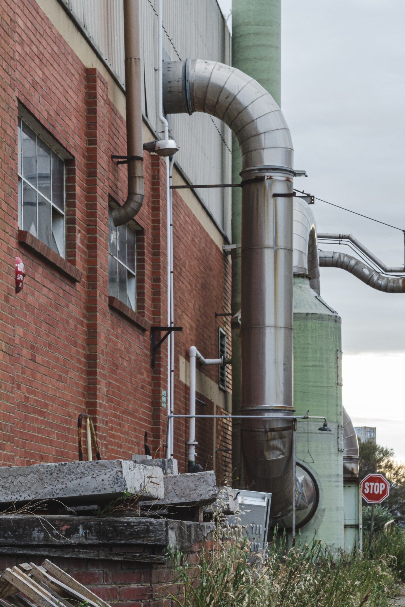Large curved metal ducting and a cylindrical stack on the exterior red brick wall of the former Bradmill factory at Yarraville, photographed in 2011.