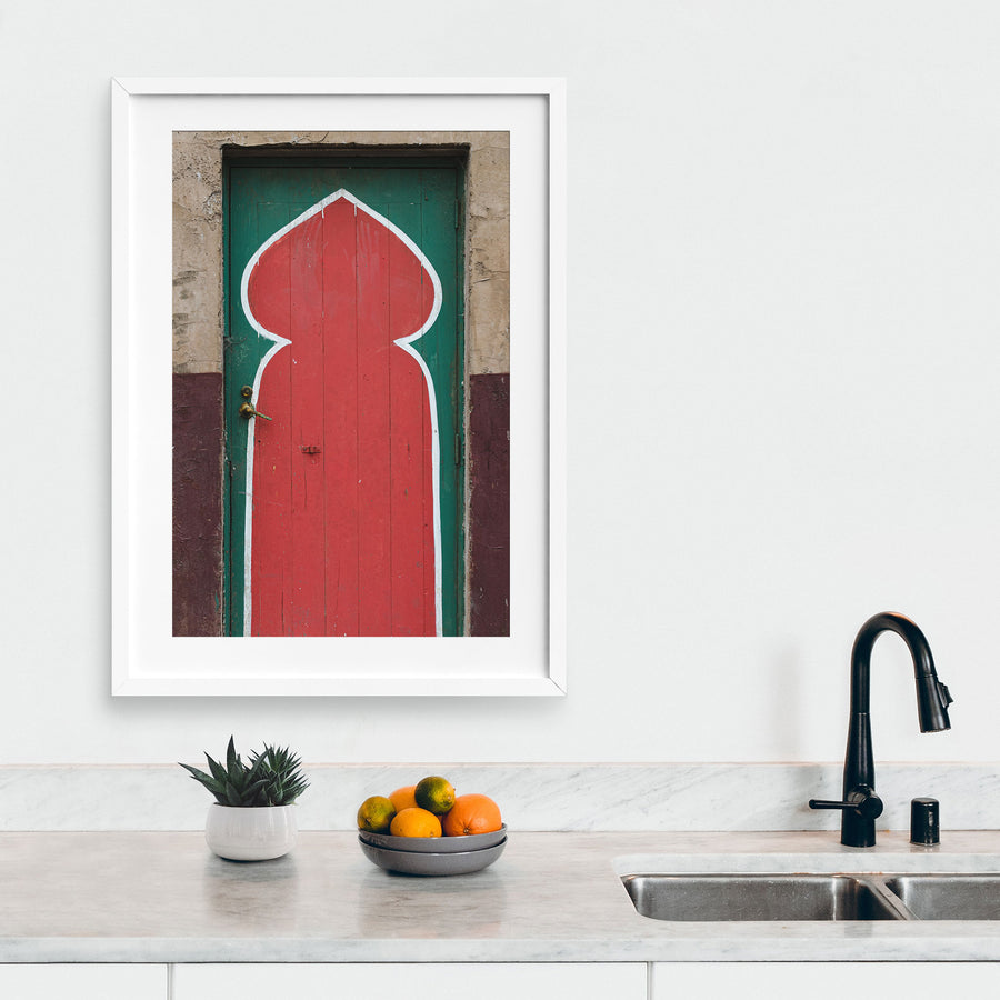 A painted timber door at the former Bradmill factory in Yarraville, with a tall red keyhole arch outlined in white on a green background, a worn brass lever handle on the left, and cracked render surrounding the frame.