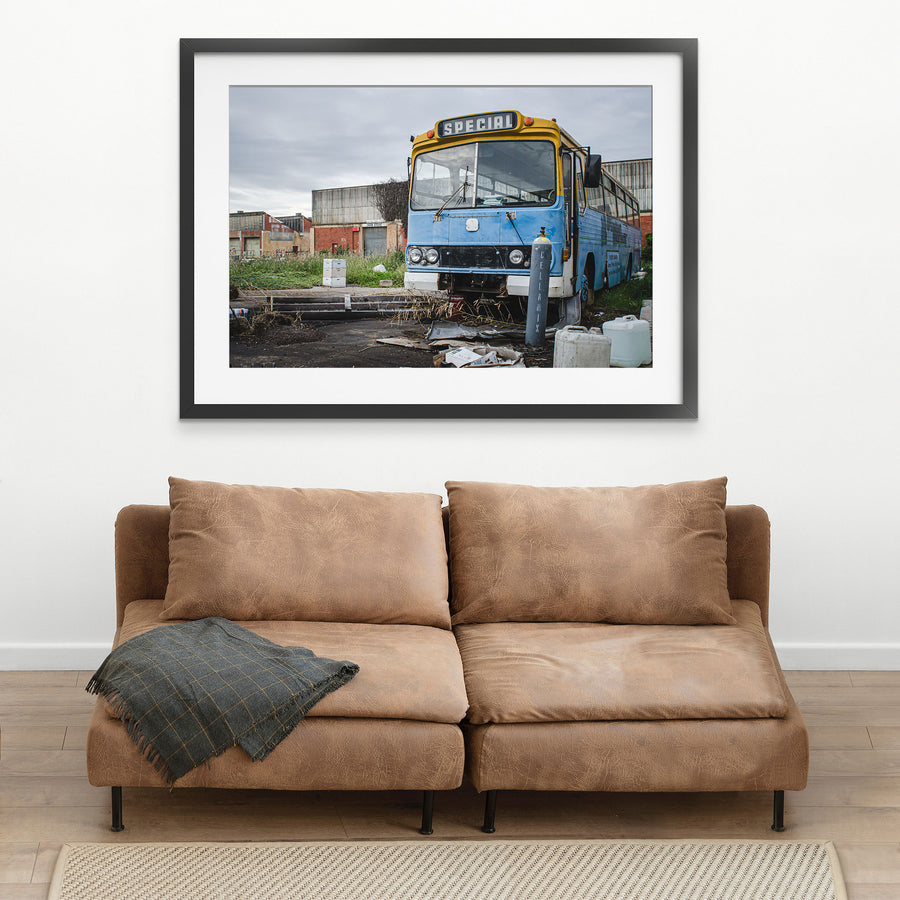 A weathered blue and yellow bus with a "Special" destination sign parked on a derelict overgrown lot at the former Bradmill factory in Yarraville, with corrugated iron and brick industrial buildings behind.