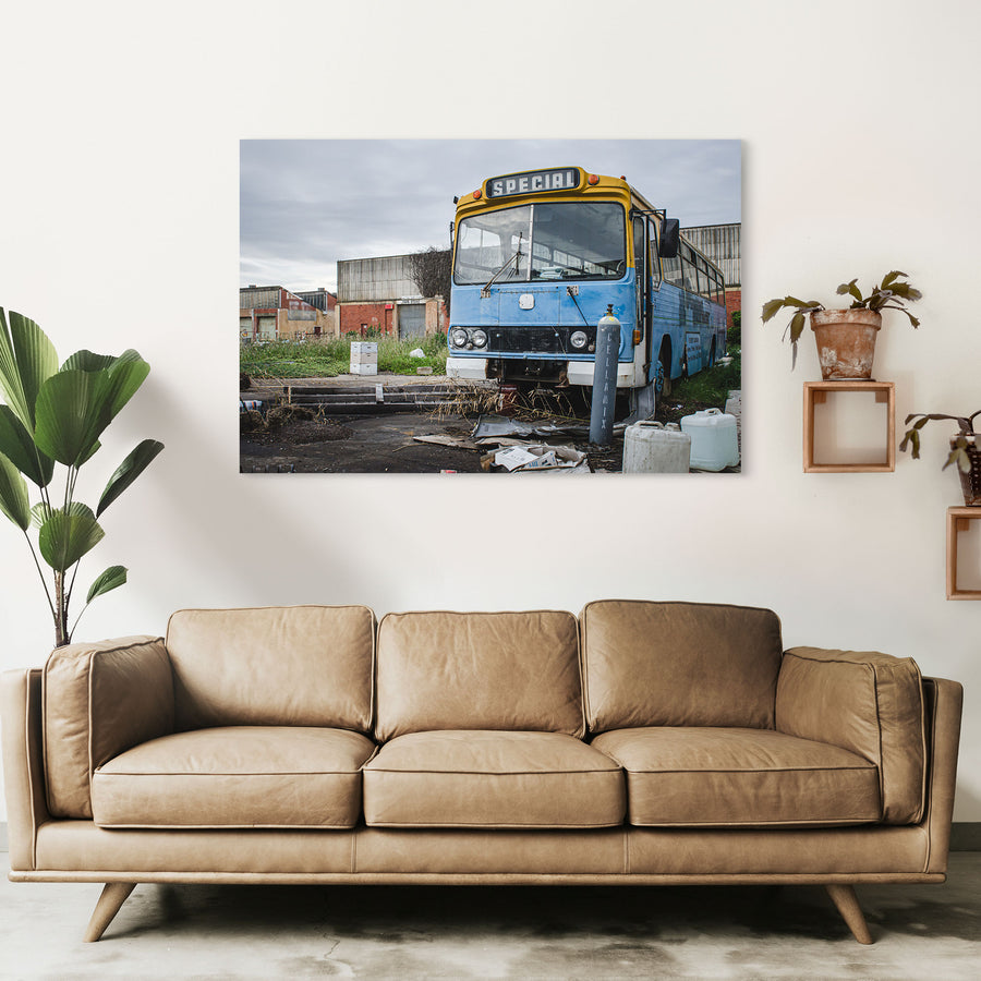 A weathered blue and yellow bus with a "Special" destination sign parked on a derelict overgrown lot at the former Bradmill factory in Yarraville, with corrugated iron and brick industrial buildings behind.