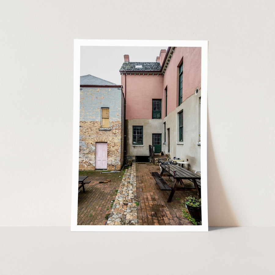 Brick courtyard with timber picnic tables, a pink-painted door and green sash windows at Braidwood Hotel, NSW.
