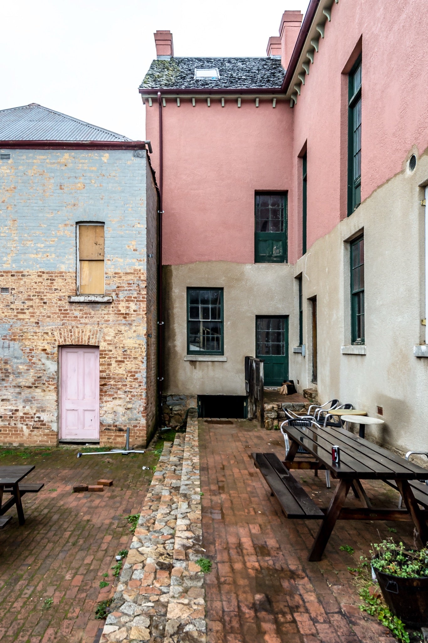 Brick courtyard with timber picnic tables, a pink-painted door and green sash windows at Braidwood Hotel, NSW.