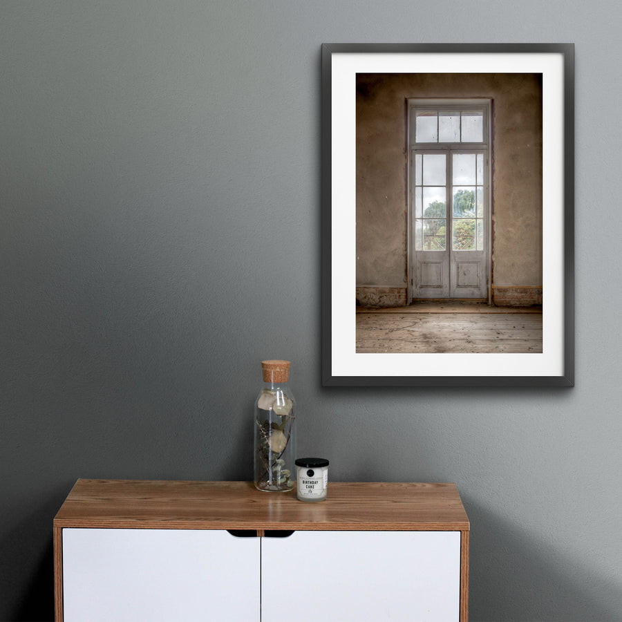 Dusty white-framed French doors with multiple glass panes and timber lower panels, set into a worn rendered wall at the Braidwood Hotel, with green trees visible beyond a timber railing.