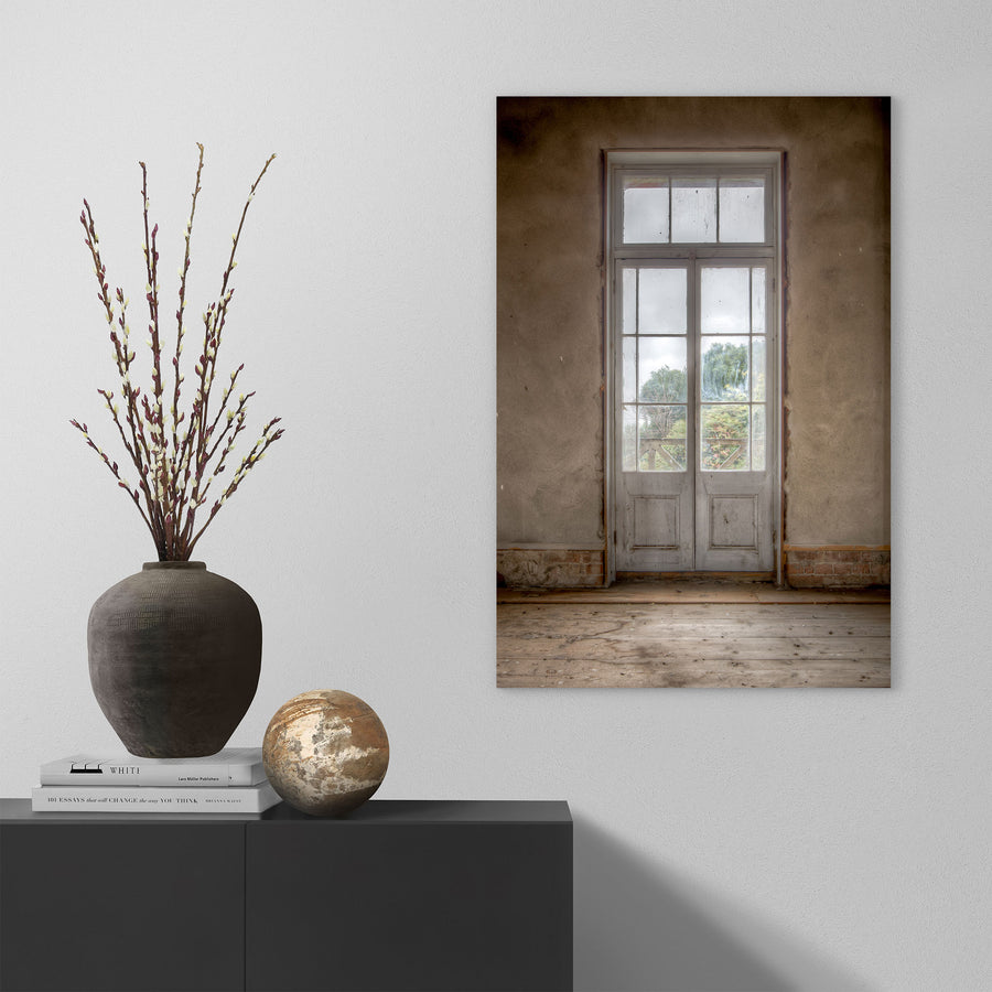 Dusty white-framed French doors with multiple glass panes and timber lower panels, set into a worn rendered wall at the Braidwood Hotel, with green trees visible beyond a timber railing.