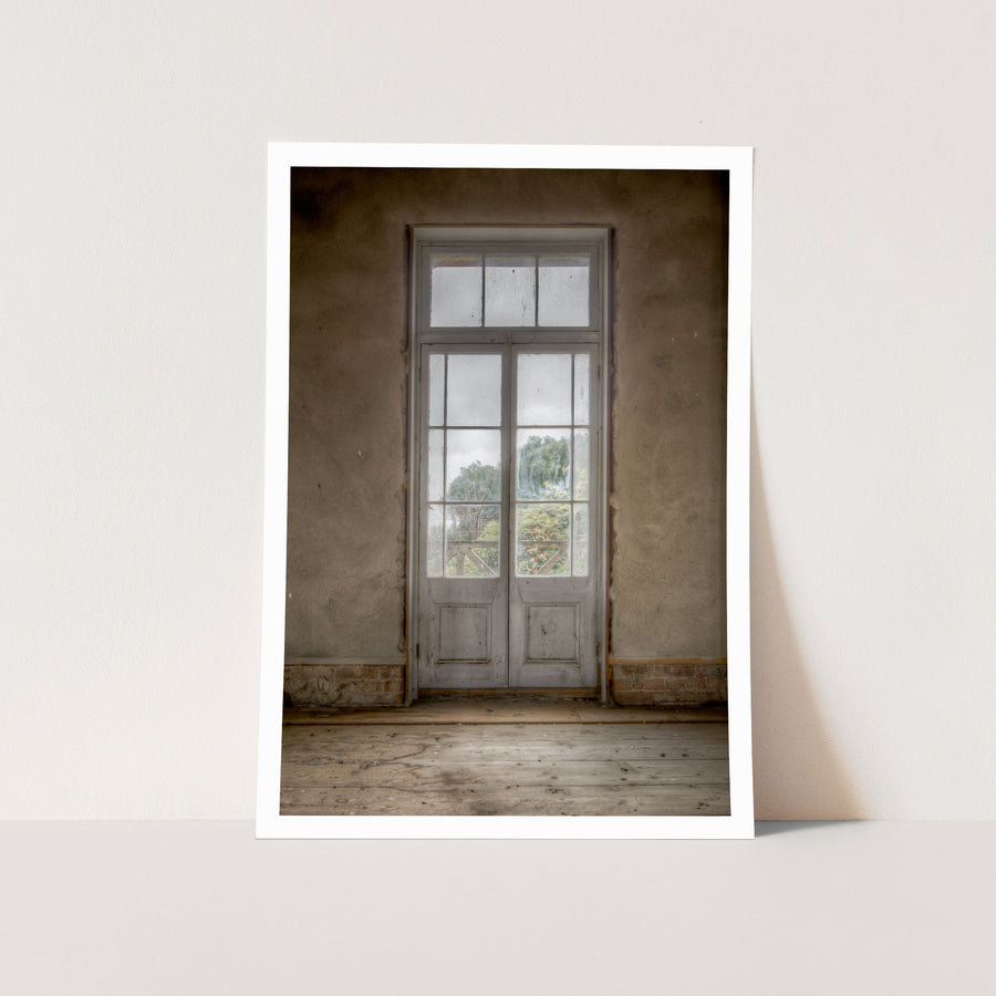 Dusty white-framed French doors with multiple glass panes and timber lower panels, set into a worn rendered wall at the Braidwood Hotel, with green trees visible beyond a timber railing.