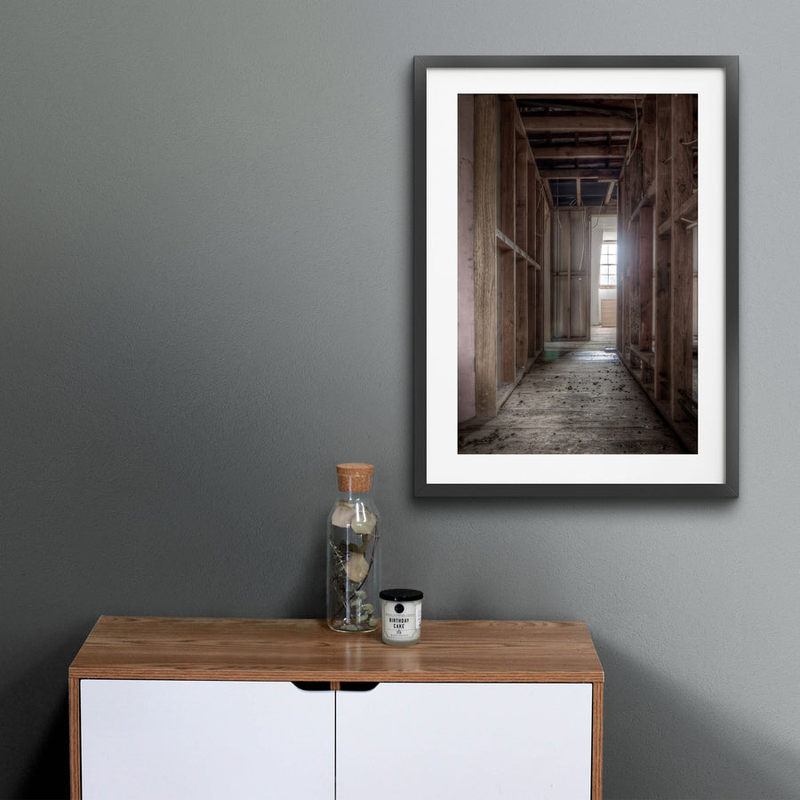 Exposed timber wall framing and ceiling joists in a stripped corridor at the Braidwood Hotel, with bare floorboards leading to a multi-pane window partially covered by plywood.