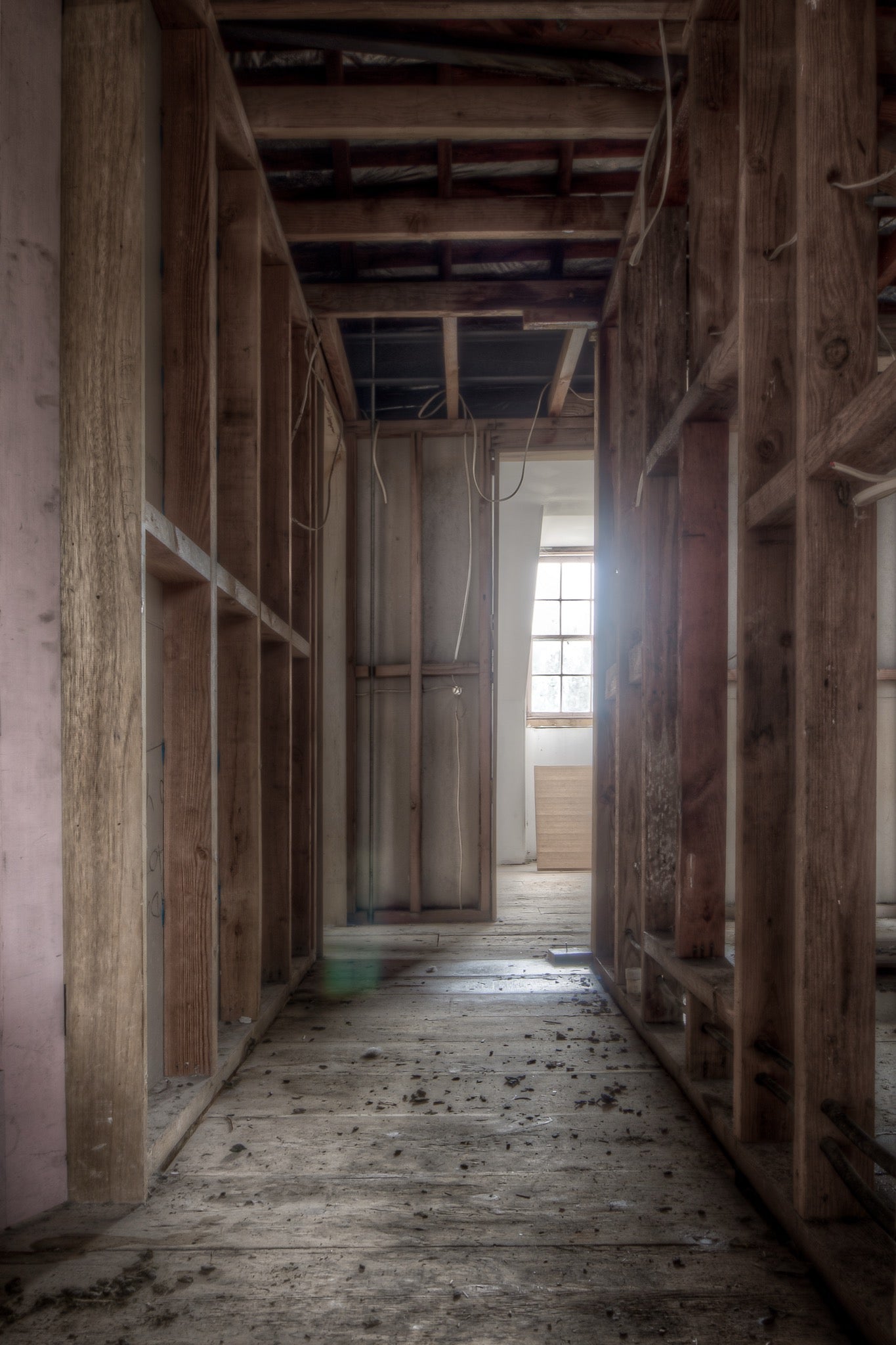 Exposed timber wall framing and ceiling joists in a stripped corridor at the Braidwood Hotel, with bare floorboards leading to a multi-pane window partially covered by plywood.
