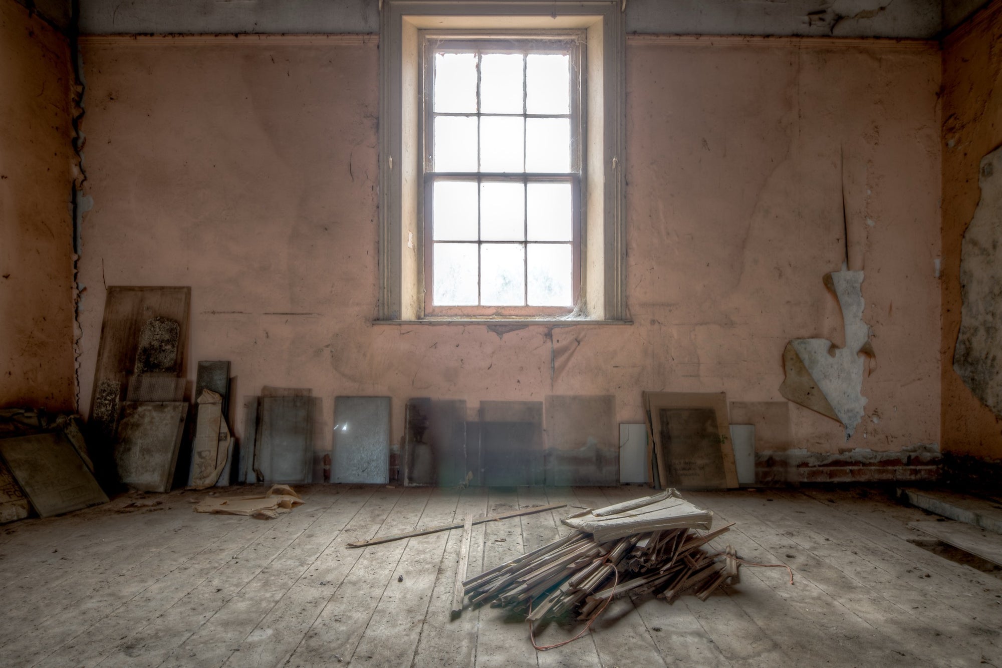 A tall multi-pane sash window in an upper room under restoration at the Braidwood Hotel, with peeling pink plaster walls and bare timber boards leaned against them.