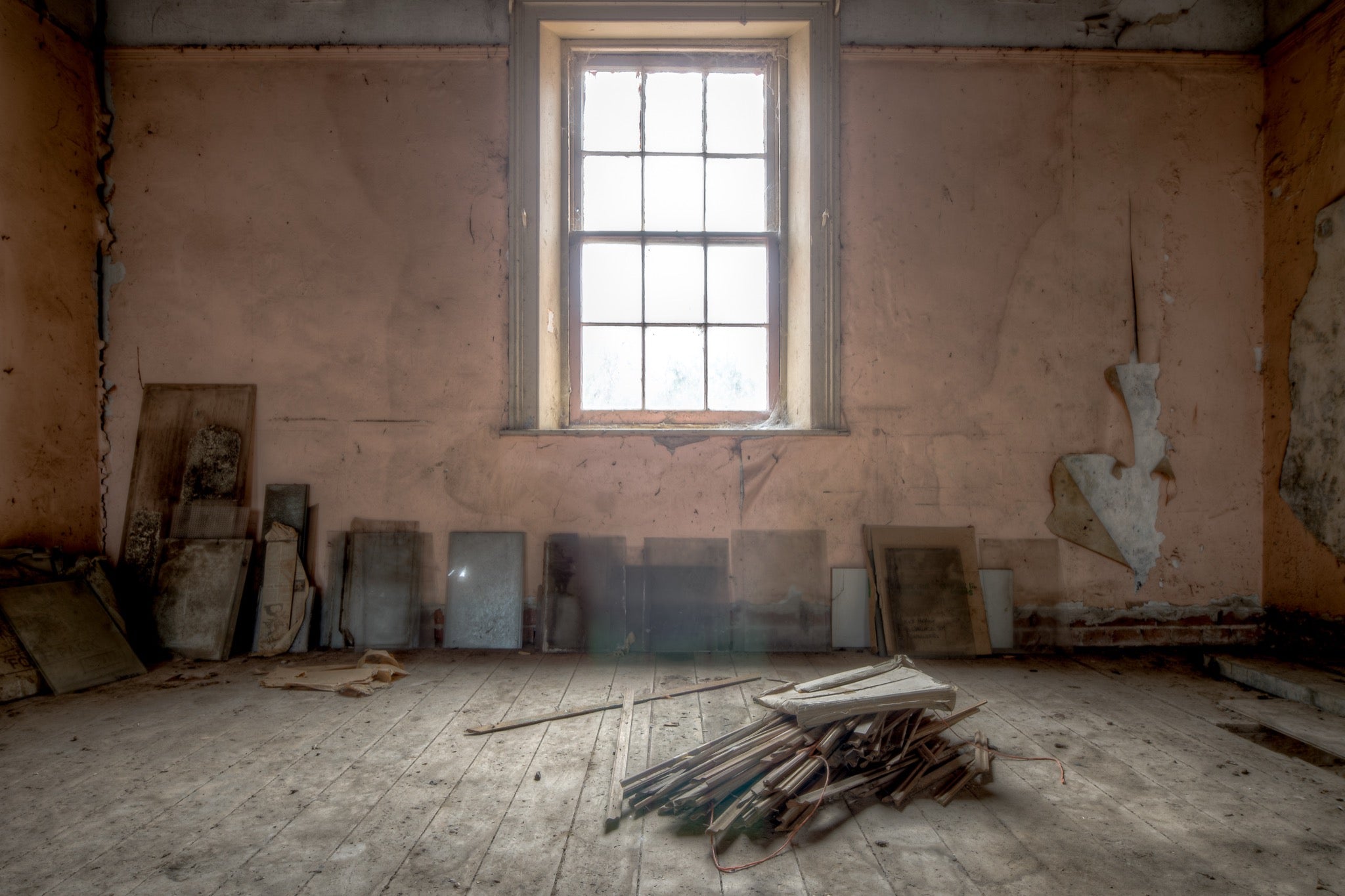 A tall multi-pane sash window in an upper room under restoration at the Braidwood Hotel, with peeling pink plaster walls and bare timber boards leaned against them.