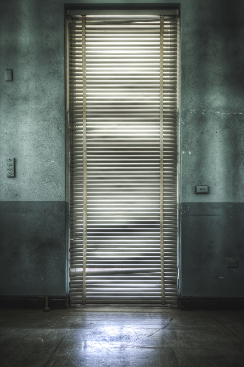 Horizontal blinds on a tall, narrow window at Callan Park break the incoming daylight into even bars across the floor.