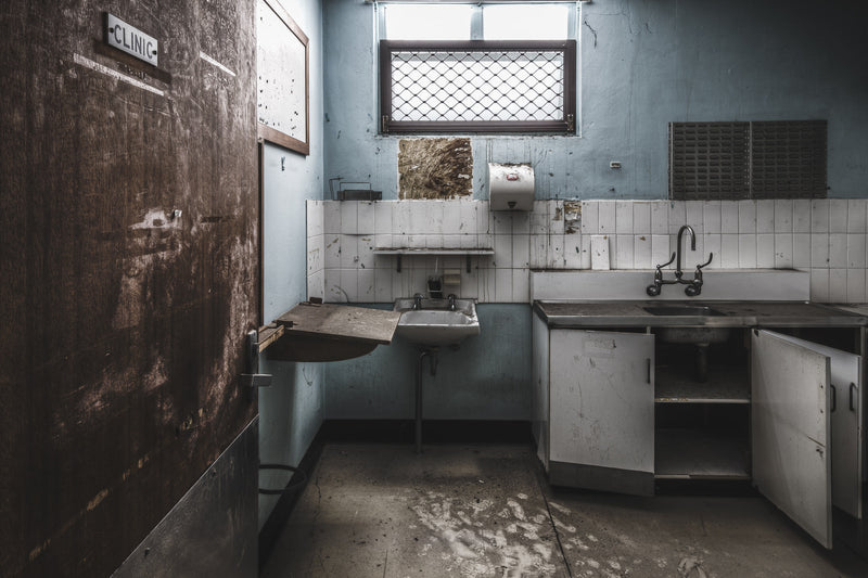 Sunlight streams through the windows of a disused clinic at Callan Park. The door marked Clinic hangs ajar, its dark timber stained and worn.