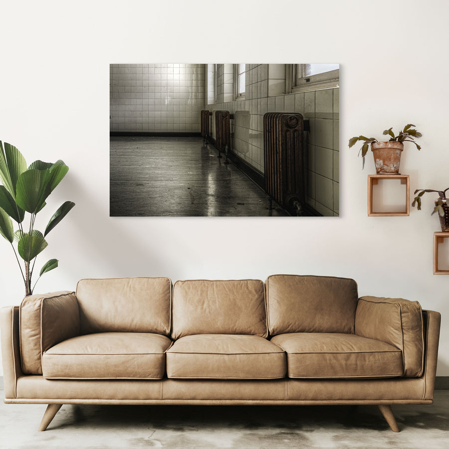 Three cast-iron radiators along a tiled corridor wall at Callan Park, reflected in the polished concrete floor below.