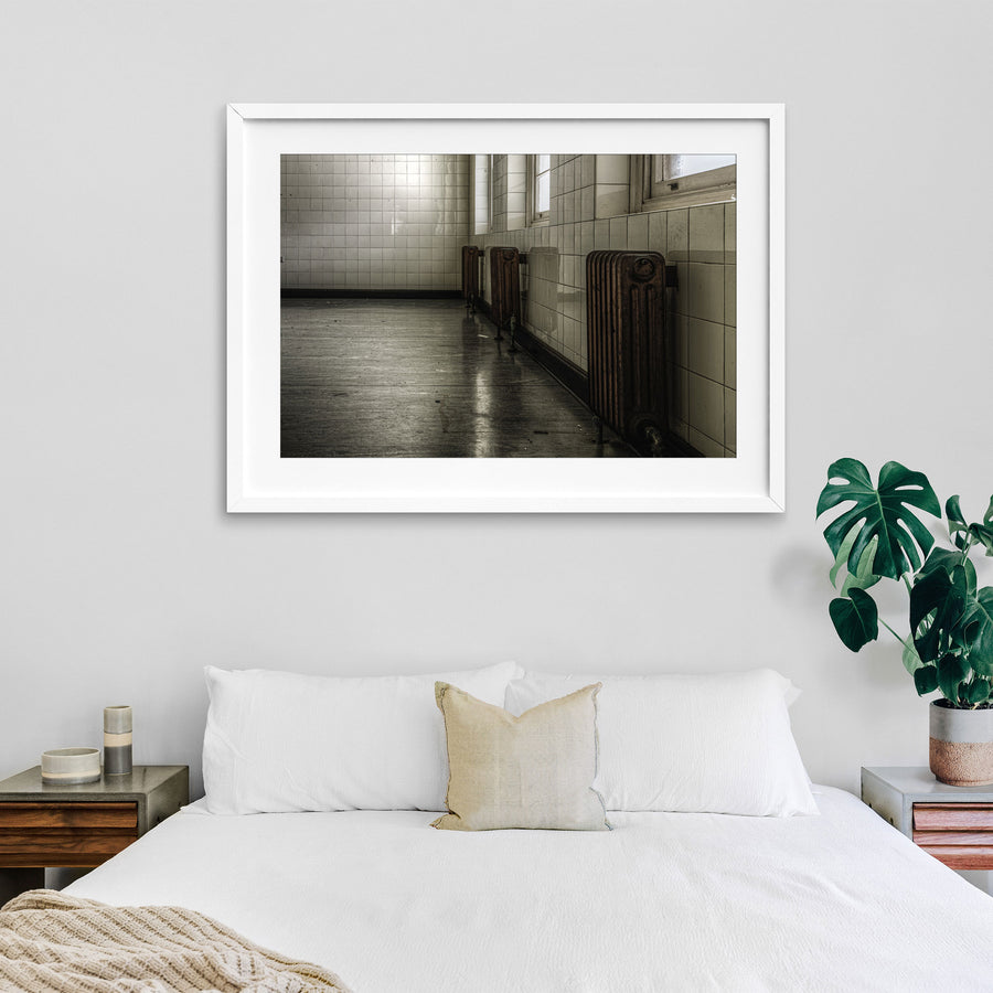 Three cast-iron radiators along a tiled corridor wall at Callan Park, reflected in the polished concrete floor below.