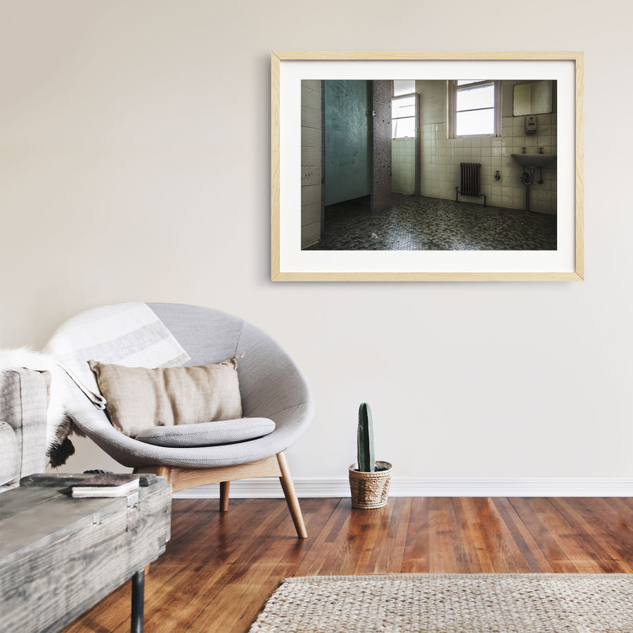 Washroom interior at Callan Park, with lifted hexagonal floor tiles, a white ceramic sink with exposed plumbing, a cast-iron radiator, and light entering through tall timber-framed windows.