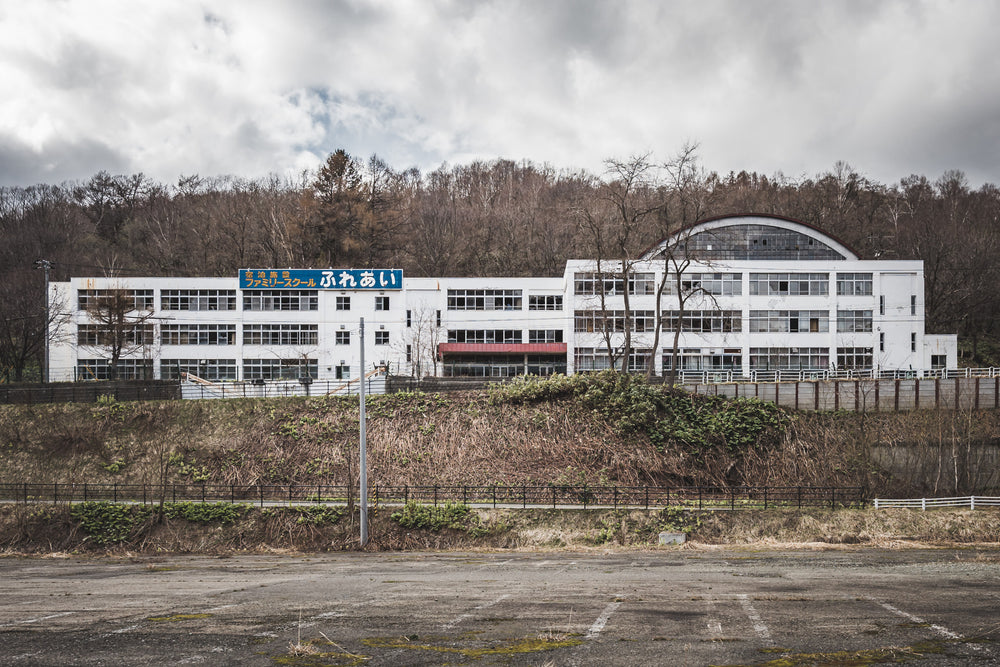 Family School Fureai at Family School Fureai, a white three-storey building sits on a raised embankment above an empty car.