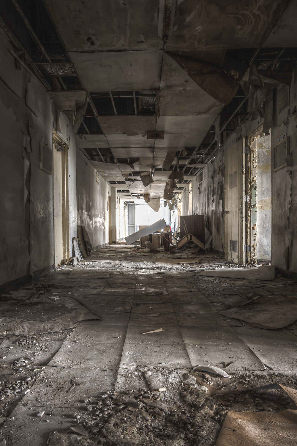 Hallway at Family School Fureai, a corridor stretches deep into the building, floor tiles buckling and separating underfoot.