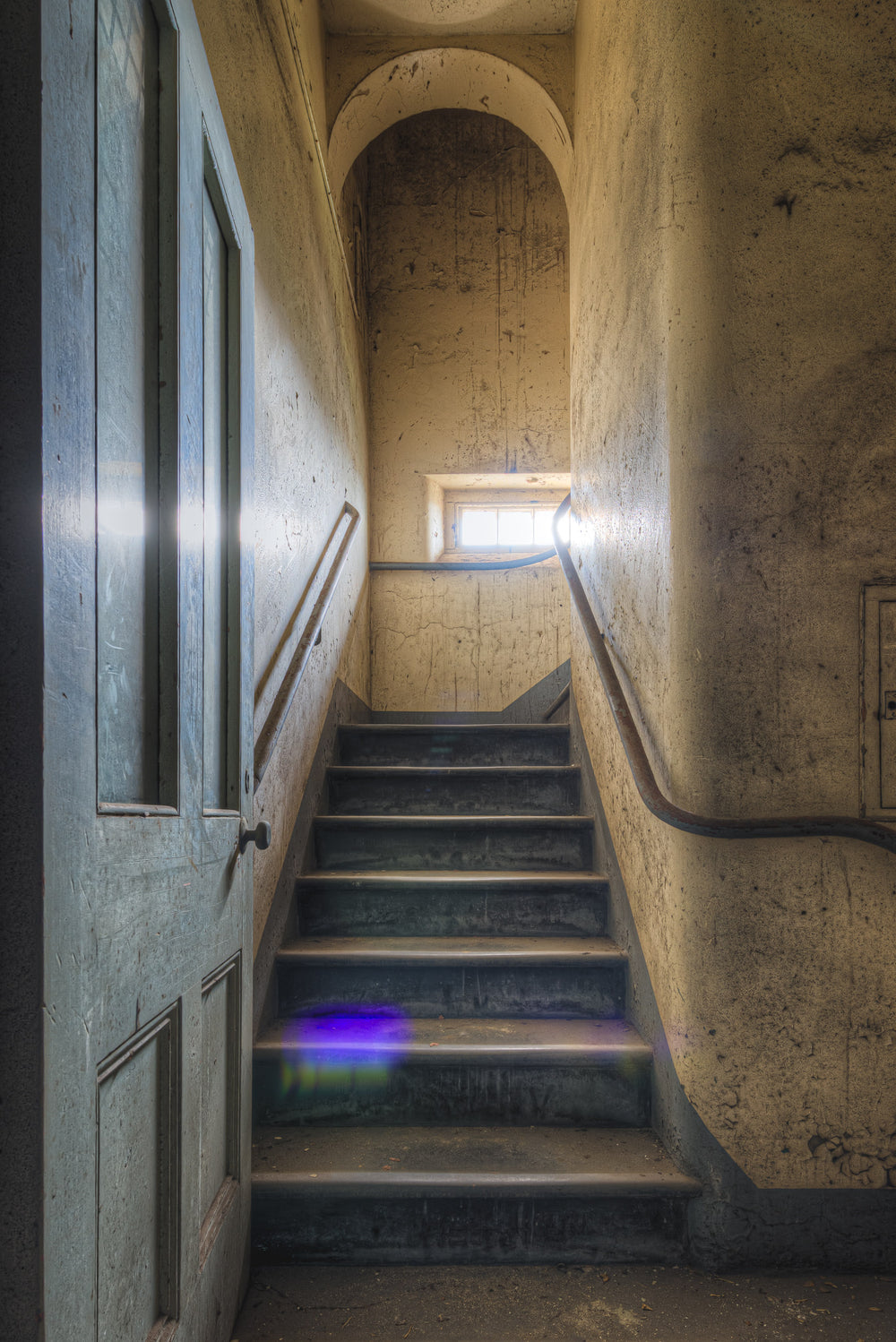 Flare at Female Ward 9 & 10, a narrow stairwell climbs between plaster walls stained grey and ochre with damp.
