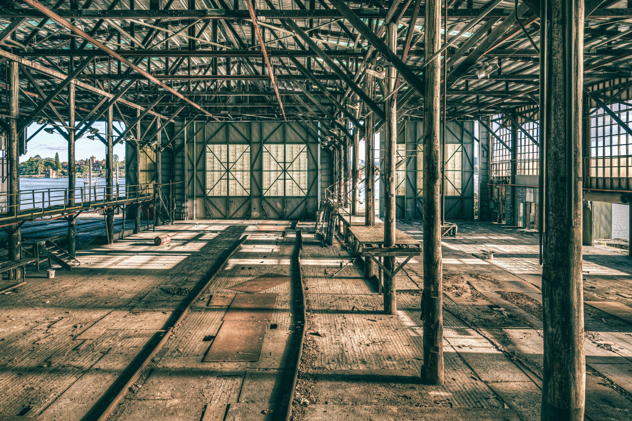 On the Catwalk at Halvorsens Boat Yard, steel columns rise from a worn timber floor, supporting a lattice of iron trusses.