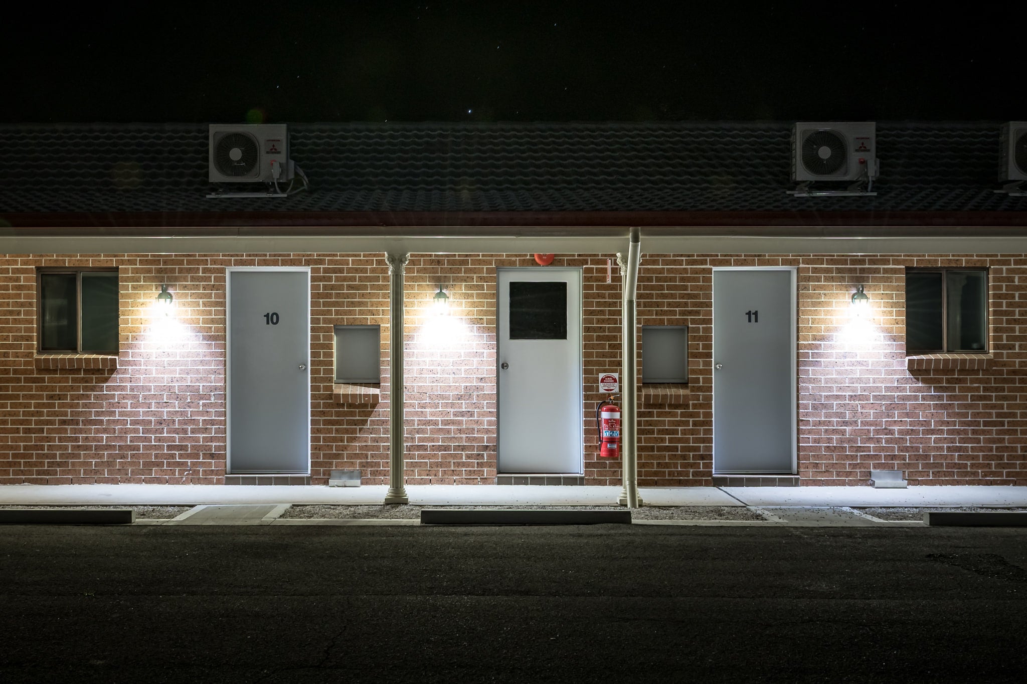 Bushmans Motor Inn at Hotel Motel 101, brown brick facade, single storey, shot dead-on at night.