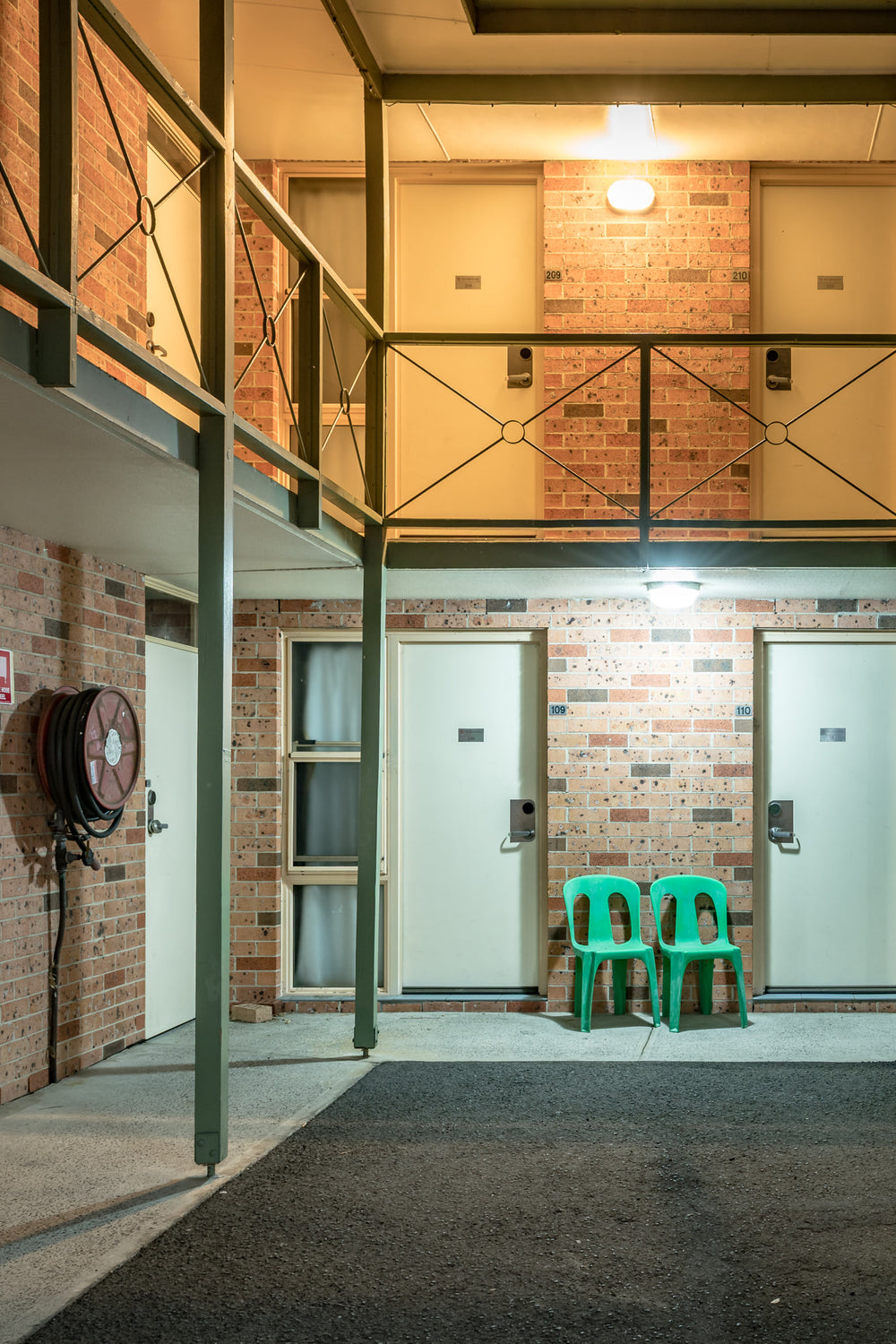 Comfort Inn Fairways at Hotel Motel 101, two green plastic chairs sit between rooms 109 and 110 on the ground floor.