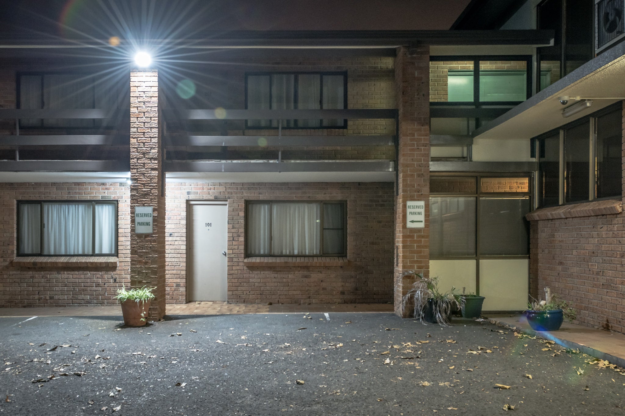 Oasis Resort at Hotel Motel 101, a single security light flares against the brick pillar between storeys, throwing hard.