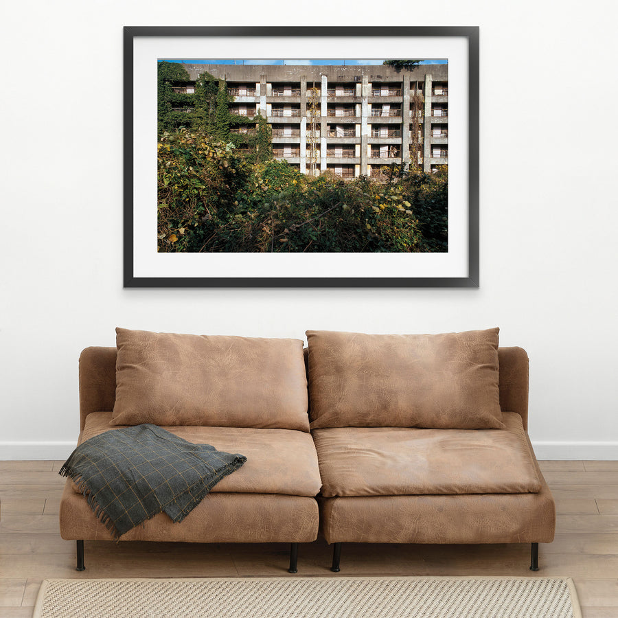 Reinforced-concrete apartment block on Ikeshima, lower storeys engulfed by green ivy and dried vines clinging to the central pillar, upper levels showing spalling and weathered balconies across five storeys.
