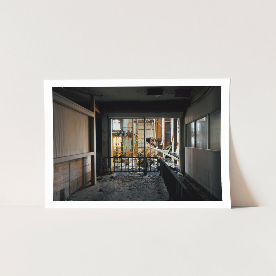 A rusted metal barrier carrying a no-entry sign blocks a doorway in a weathered interior at Ikeshima, with collapsed steelwork and broken pipes visible beyond in bright sunlight.