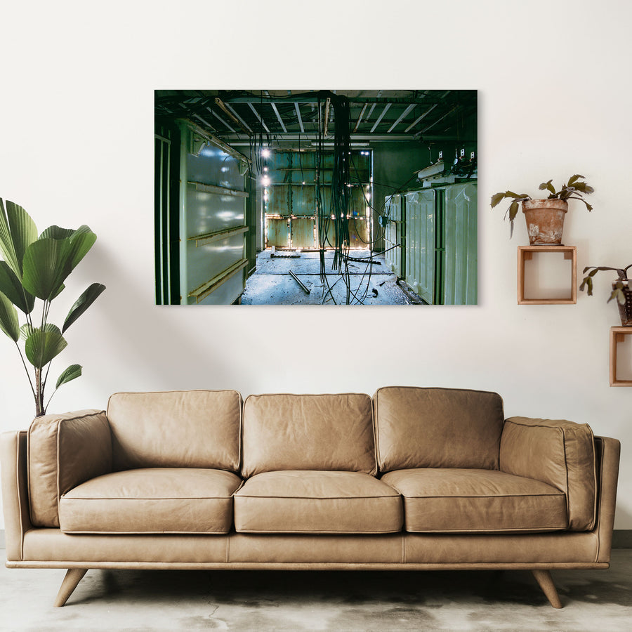 Dense black cable bundle hanging from an exposed ceiling frame runs the length of a corridor at Ikeshima Coal Mine, with two ribbed transformers along one wall and teal double doors at the far end.