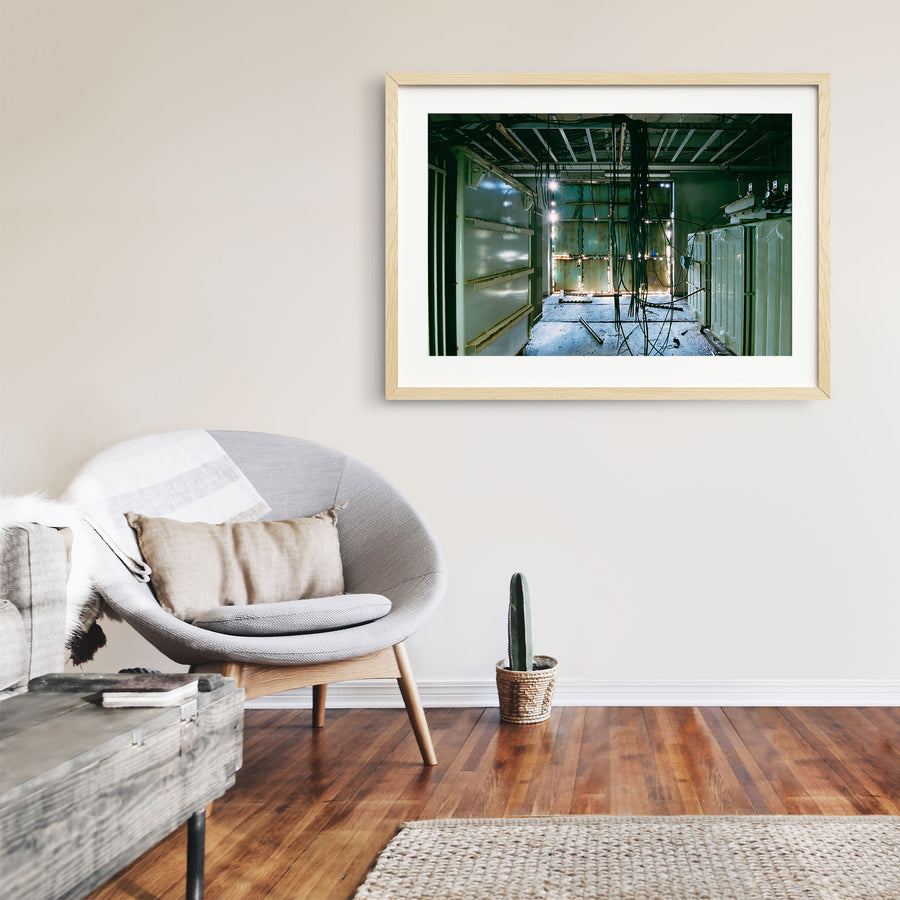 Dense black cable bundle hanging from an exposed ceiling frame runs the length of a corridor at Ikeshima Coal Mine, with two ribbed transformers along one wall and teal double doors at the far end.