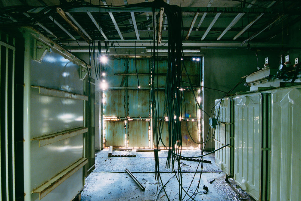 Transformer room in the winder house at Ikeshima Coal Mine, cream steel casings either side of an aisle with severed cables hanging.