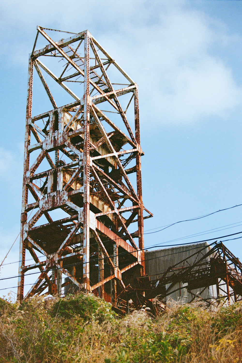 No. 1 shaft headframe at Ikeshima Coal Mine seen from its foot, rusted lattice tower filling the frame against blue sky.