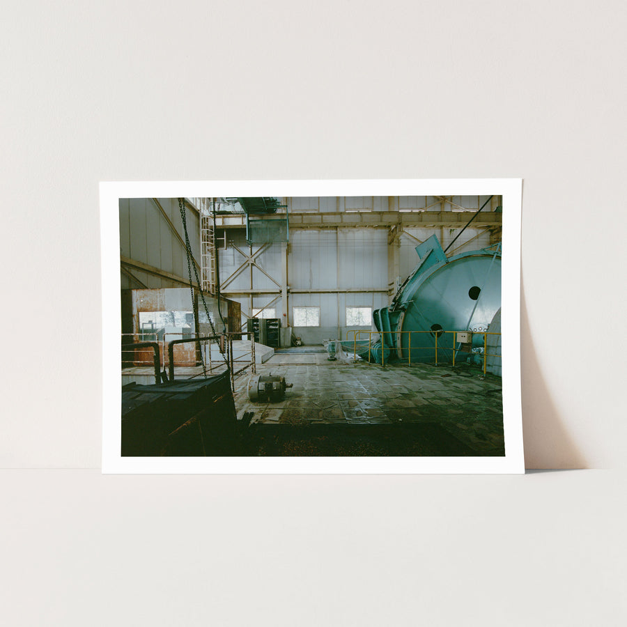The sheave wheel, hoist drum and hanging chains of the winding house interior at Ikeshima Coal Mine, with a yellow-railed cylindrical vessel to the right and three rectangular windows along the far wall.