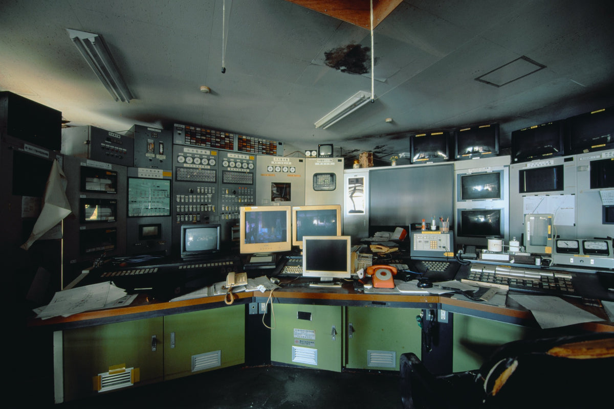 Curved operator console with three beige CRT monitors, orange rotary telephones and instrument panels at the Ikeshima Coal Mine control room.
