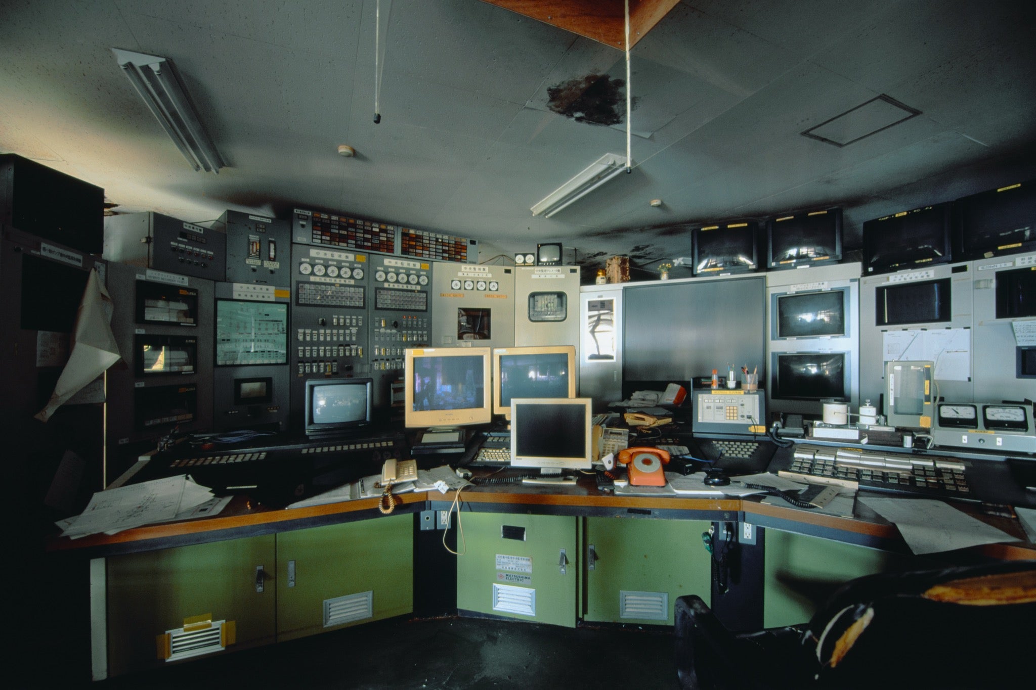 Curved operator console with three beige CRT monitors, orange rotary telephones and instrument panels at the Ikeshima Coal Mine control room.