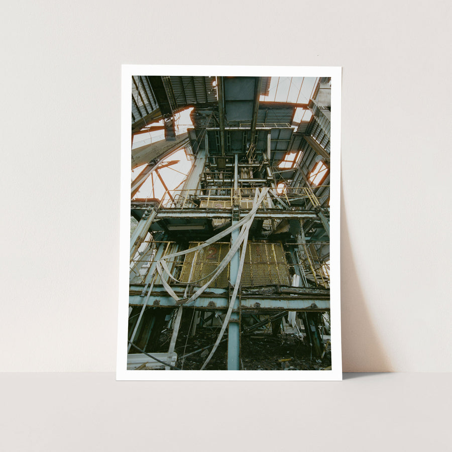 Corroded steel framing and two numbered yellow mesh barrier panels inside the main mining building at Ikeshima Coal Mine, with white fabric hanging loosely across them and daylight entering through holes in the corrugated roof above.