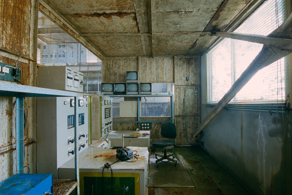 Winder control room at Ikeshima Coal Mine, rusted control desk with a telephone and stacked CRT monitors under louvred blinds.