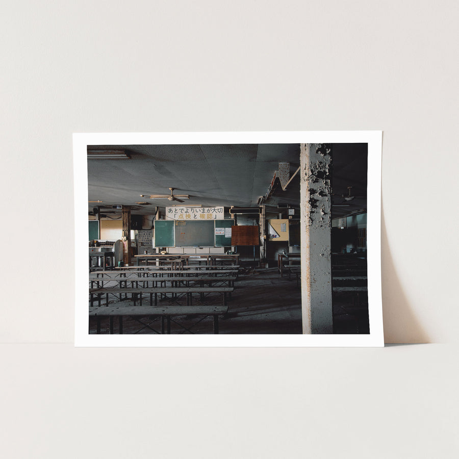 A dust-covered briefing room at Ikeshima Coal Mine, with rows of wooden tables and bench seating facing two dark green chalkboards, a rotary telephone on a table, and a safety sign on the rear wall carrying Japanese text.