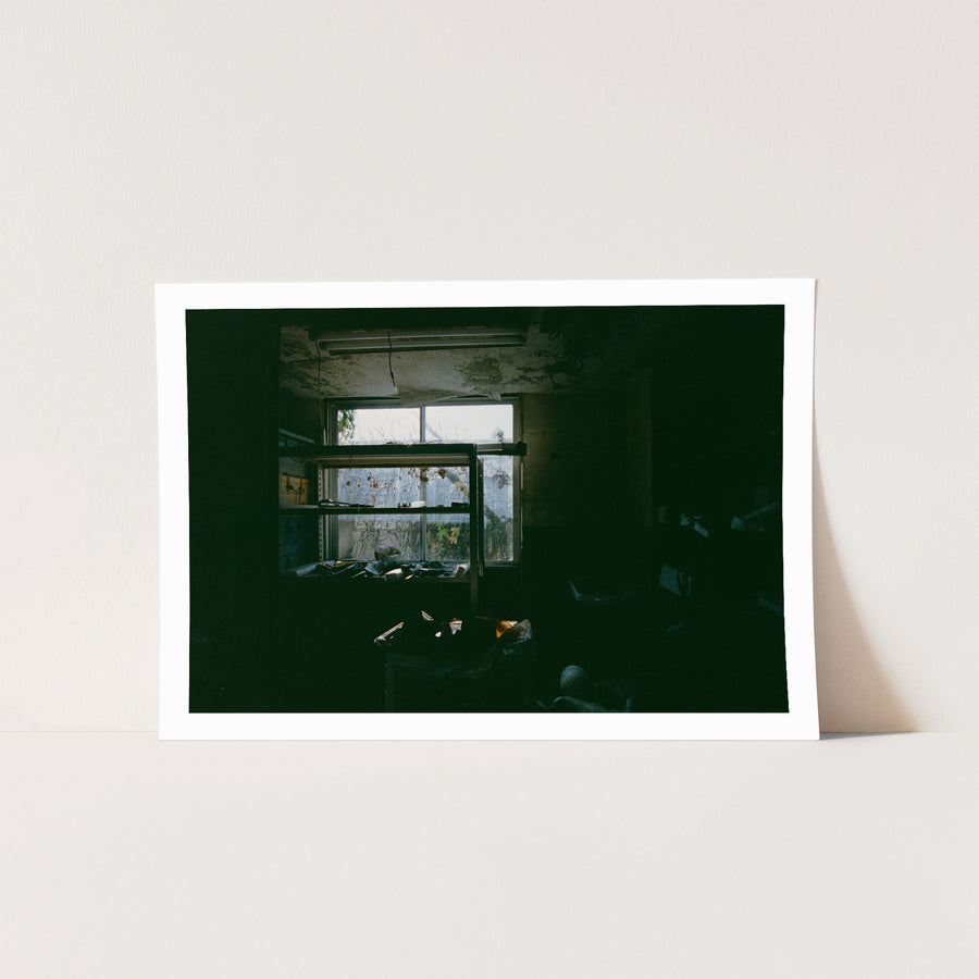 A metal shelving unit stands before a multi-pane window at Ikeshima Coal Mine, vines pressing against the grimy glass outside, with papers and ceramic objects scattered across the shelves and floor.