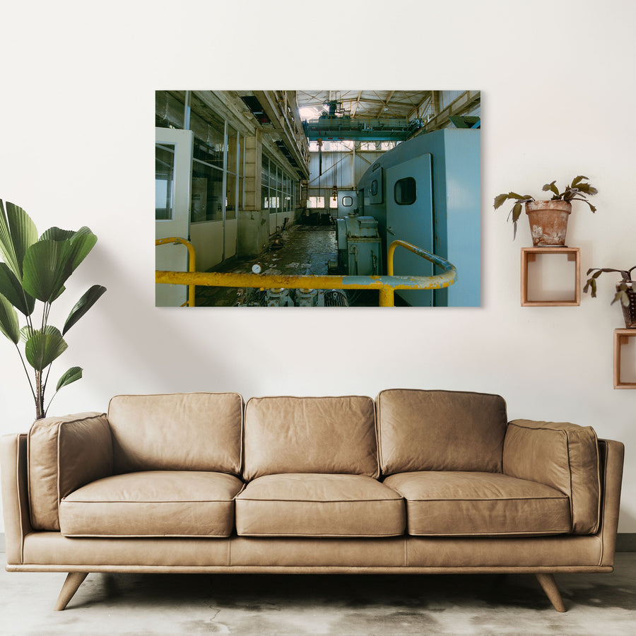 Interior of the winding house at Ikeshima Coal Mine, showing a light-blue winding engine with panelled doors, a teal overhead gantry crane, glass-paned windows, and a pressure gauge on the concrete floor.