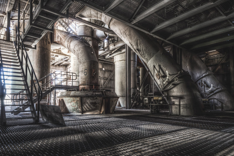 Inside Kandos Cement Works, a cyclonic separator dominates the frame. Its vast, corroded steel structure and complex pipework carry rust and accumulated grime in every joint and seam.