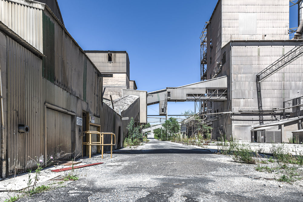 Looking South at Kandos Cement Works, a cracked internal road runs south between a corrugated iron shed and a massive.
