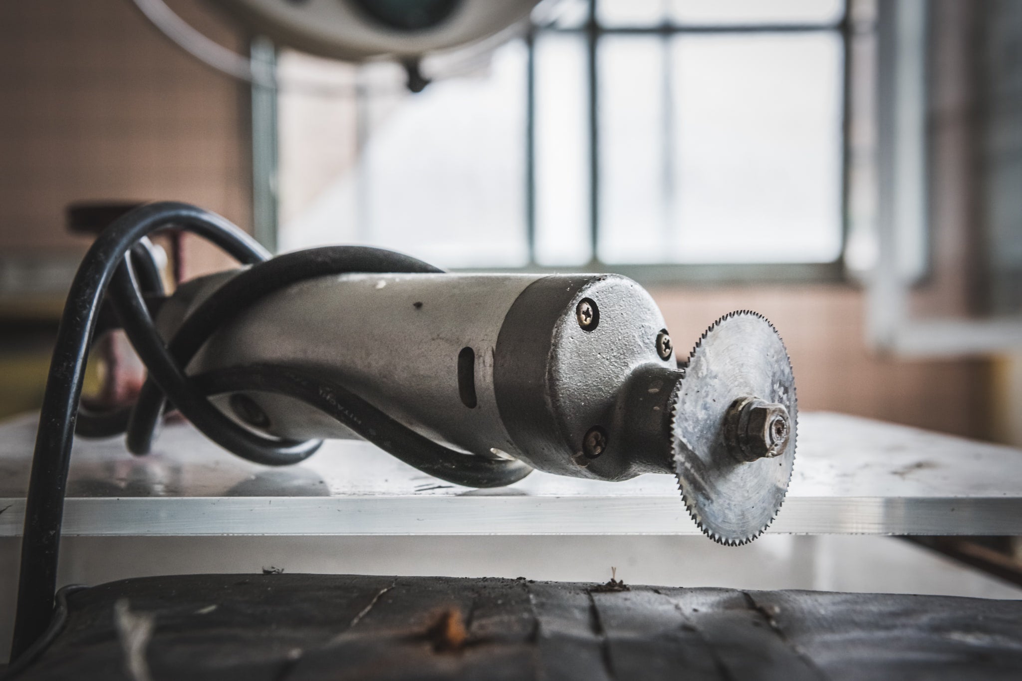 Bone Saw at Kuwashima Hospital, a cast-cutting saw rests on a metal surface, its small circular blade still fitted.